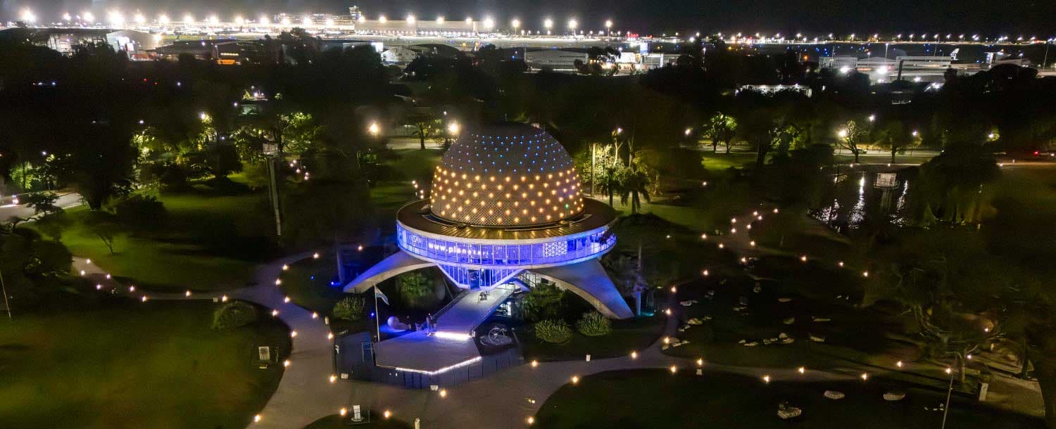 The illuminated dome of the Galileo Galilei Planetarium and surrounding park at night.